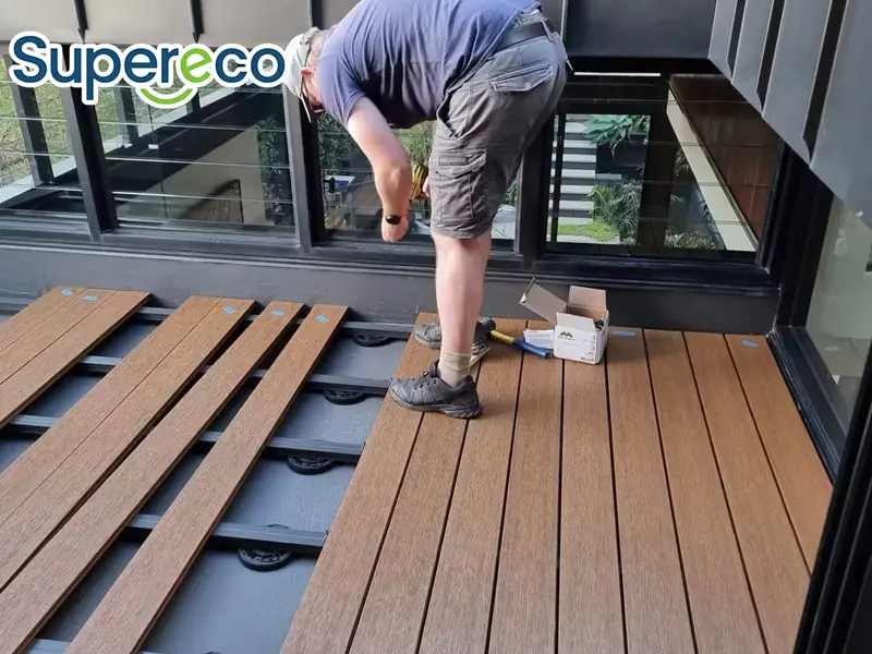 A contractor installs durable composite decking boards on a raised commercial balcony using a hidden fastener system, sourced from a wholesale supplier.